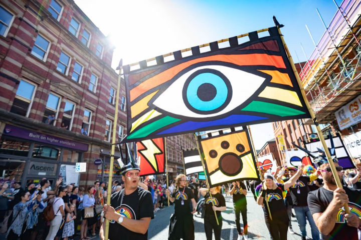 People with painted faces holding a colourful banner while marching in the street