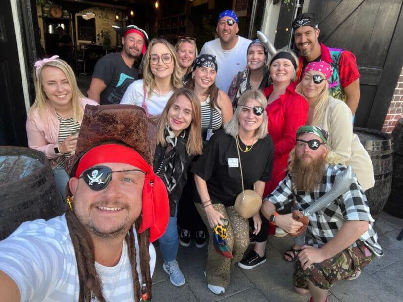 A large group of workmates, dressed up as pirates with inflatable swords, out on a treasure hunt